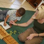 A teacher is assisting a little boy to write with number blocks